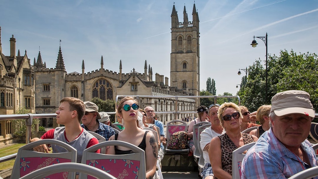 Open-top bus tour with tourists viewing historic Oxford architecture.