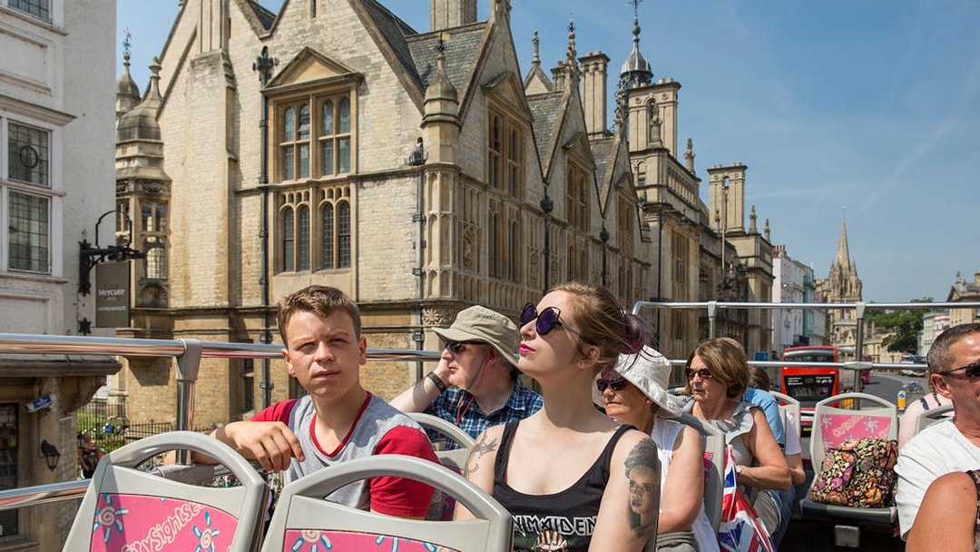 Open-top bus tour passing historic buildings in Oxford.