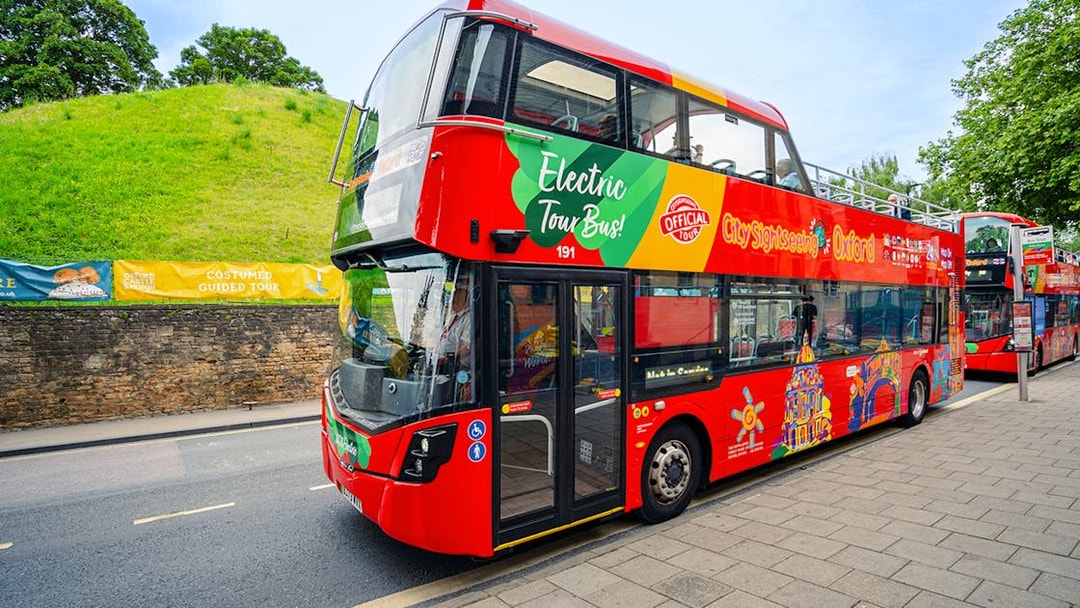 Oxford sightseeing bus passing historic building.