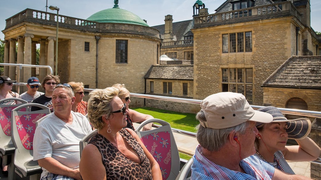 Tourists on an open-top bus during a 24/48-Hr Hop-On Hop-Off Tour of Oxford, passing historic buildings.