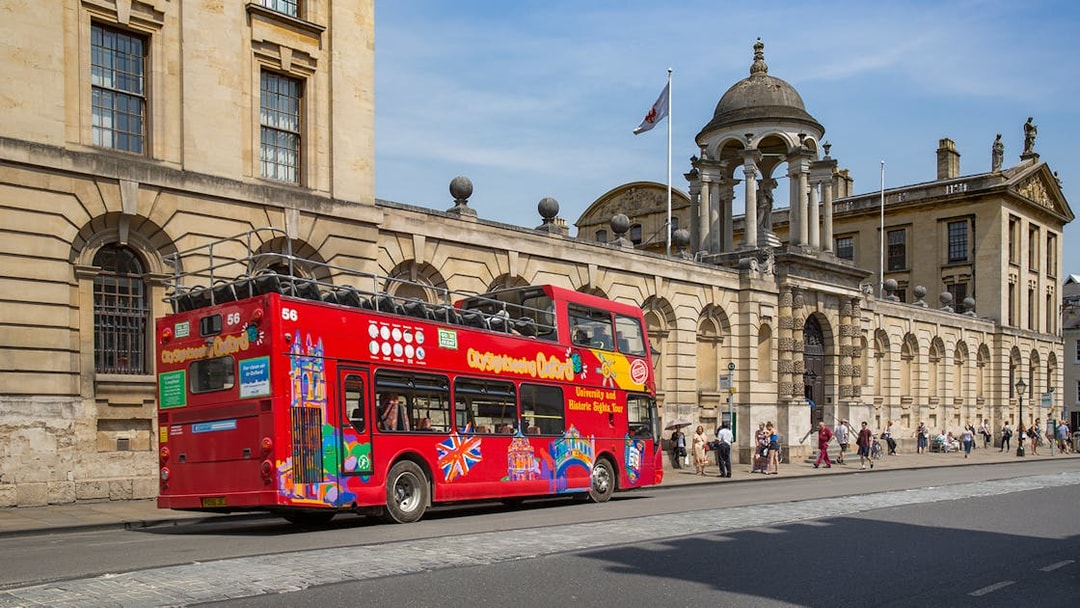 Red double-decker bus on Oxford street near historic building, part of 24/48-Hr Hop-On Hop-Off Tour.