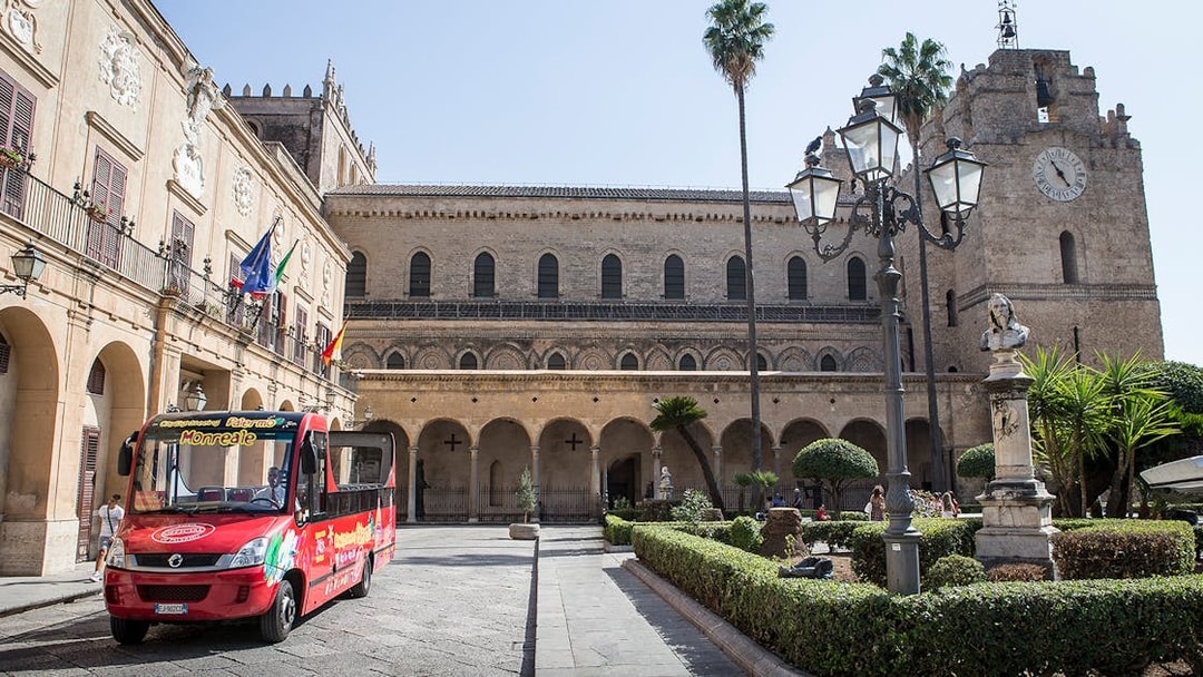 Palermo hop-on hop-off bus in front of historic building with clock tower.
