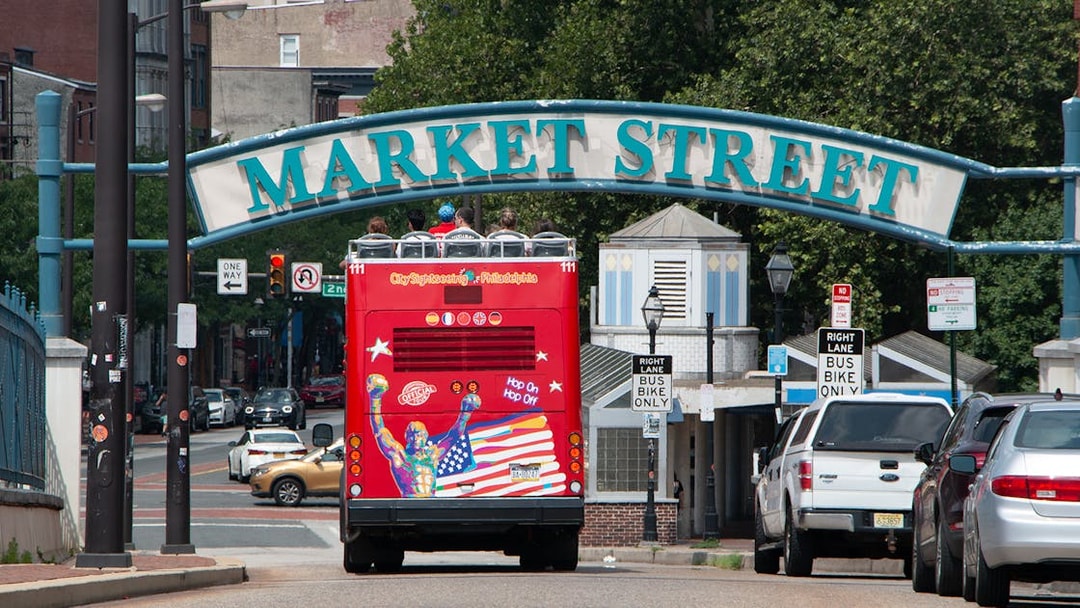 Red double-decker bus on Philadelphia Hop-On-Hop-Off Tour passing under Market Street sign.