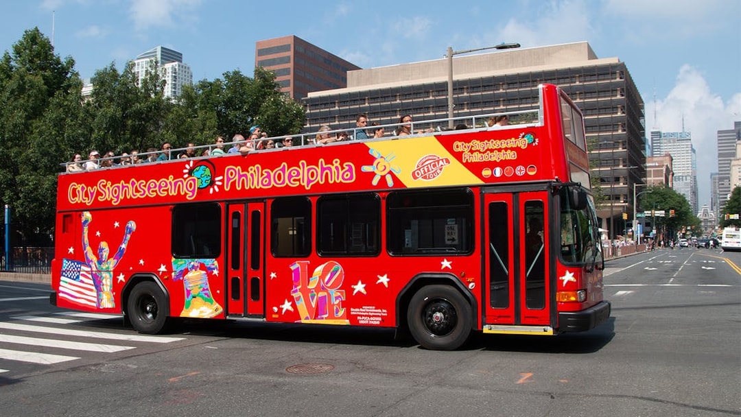 Red double-decker bus on Philadelphia Hop-On-Hop-Off Tour with city buildings in background.
