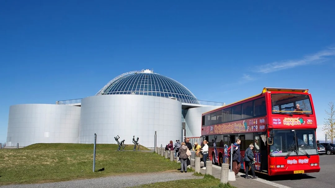 Reykjavik hop-on hop-off bus near Perlan with tourists boarding.