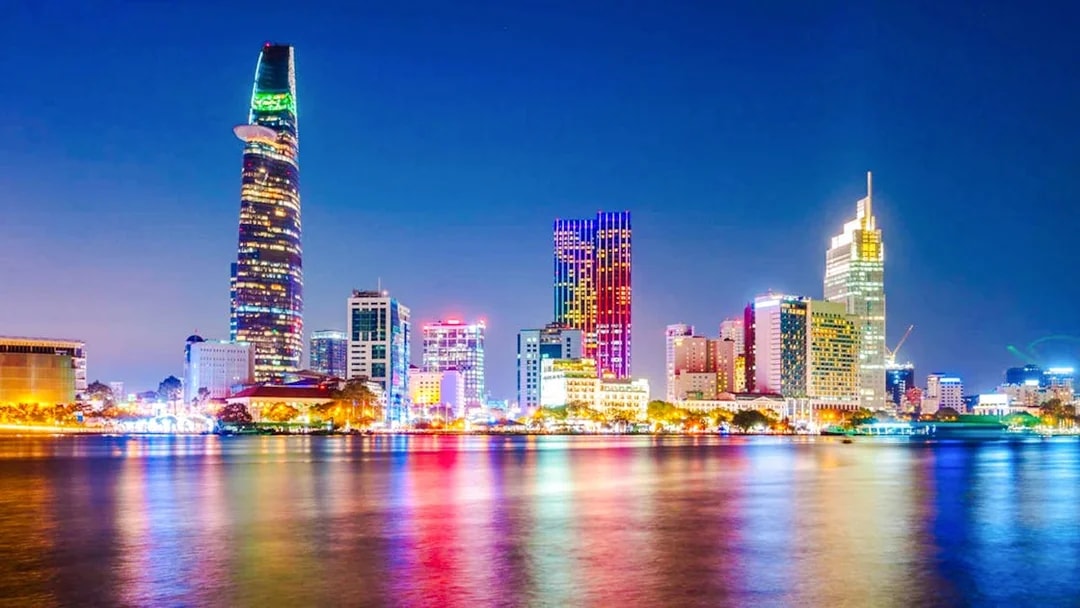 Saigon cityscape at night with illuminated skyscrapers reflecting on the river.
