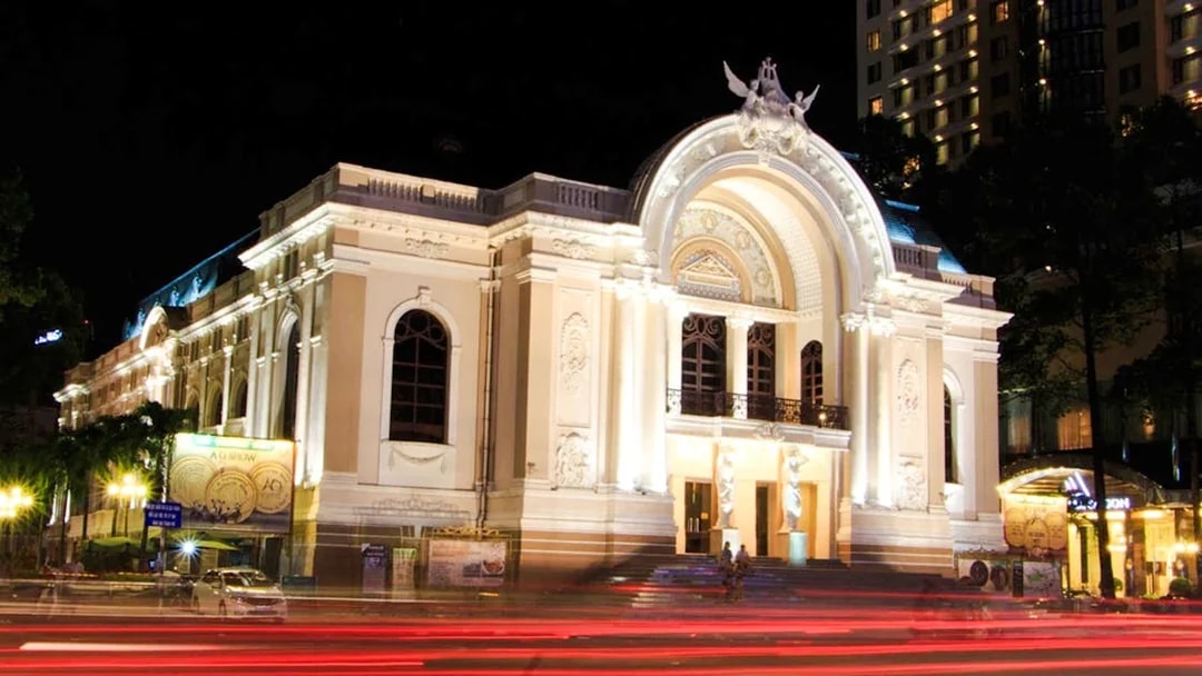 Ho Chi Minh Municipal Theater illuminated at night with light trails from passing traffic.