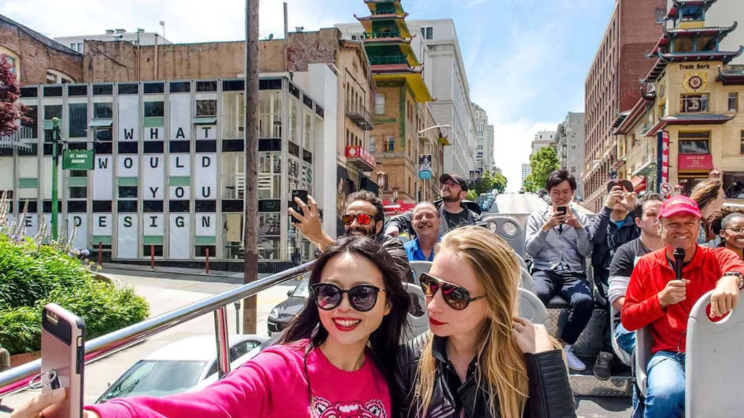 Open-top bus tour in San Francisco's Chinatown with tourists taking photos.