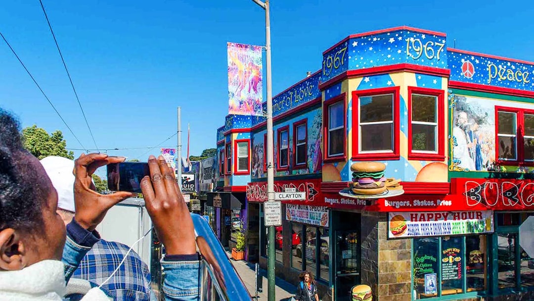 Tourists on a San Francisco hop-on hop-off bus photographing colorful Haight-Ashbury murals.