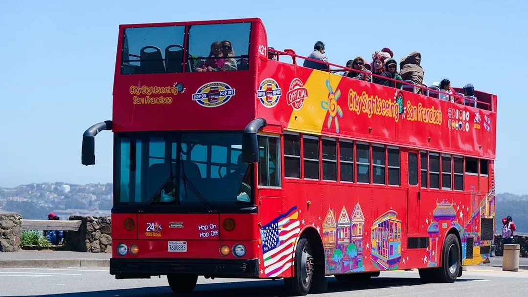 Red double-decker sightseeing bus in San Francisco with tourists on top deck.