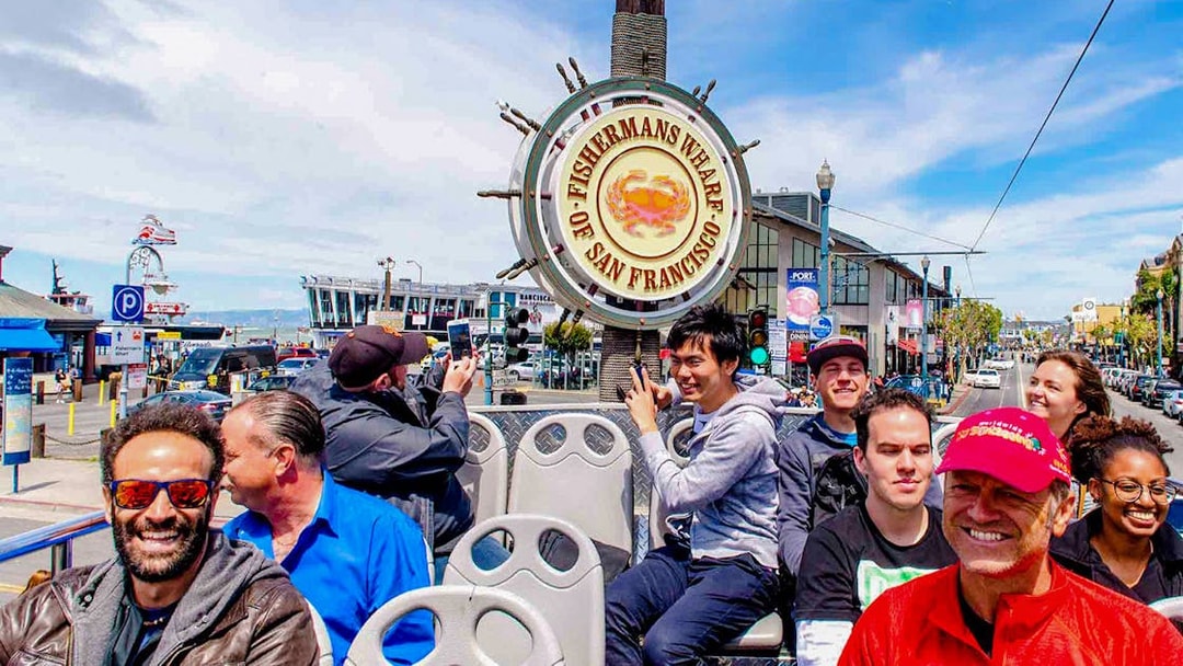 Open-top bus tour at Fisherman's Wharf, San Francisco, with tourists enjoying the view.