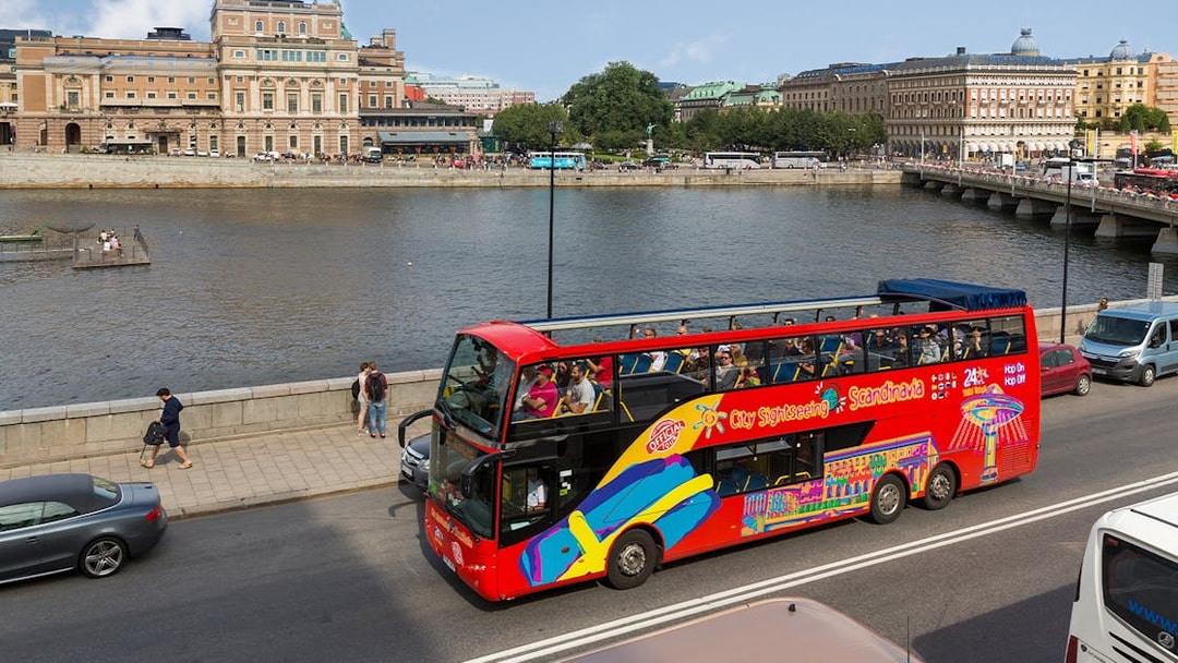 Open-top sightseeing bus near Stockholm waterfront and historic buildings.