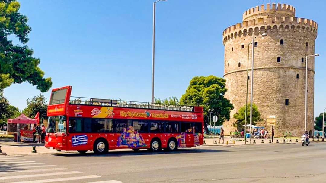 Red double-decker bus near the White Tower on Thessaloniki Hop-On-Hop-Off Tour.