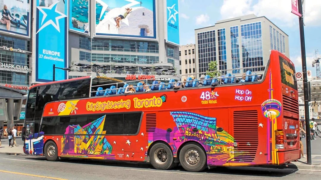 Open top Toronto Hop-On Hop-Off bus near city billboards.