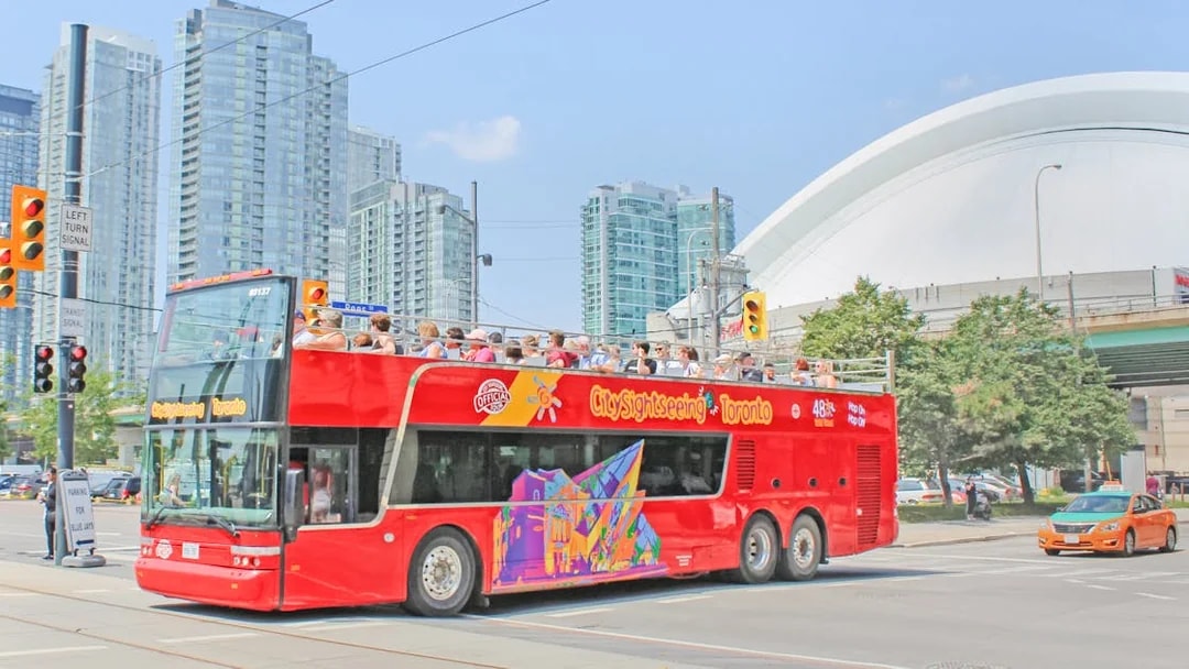 Tourists on a City Sightseeing bus exploring Toronto with CN Tower in the background.