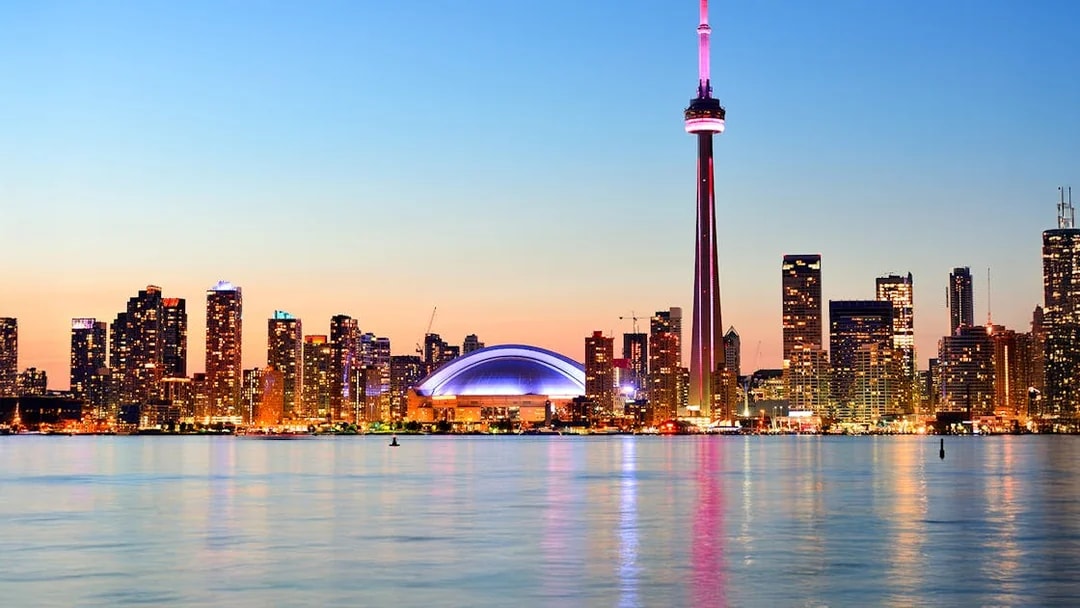 Toronto skyline with CN Tower at sunset reflecting on Lake Ontario.