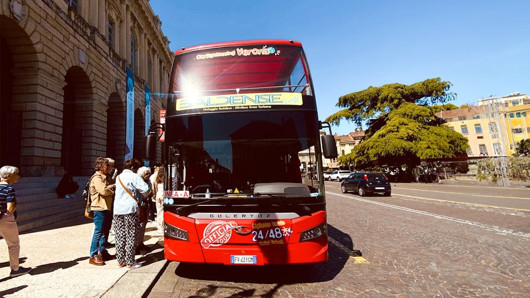 Verona hop-on hop-off tour bus with passengers boarding near historic buildings.