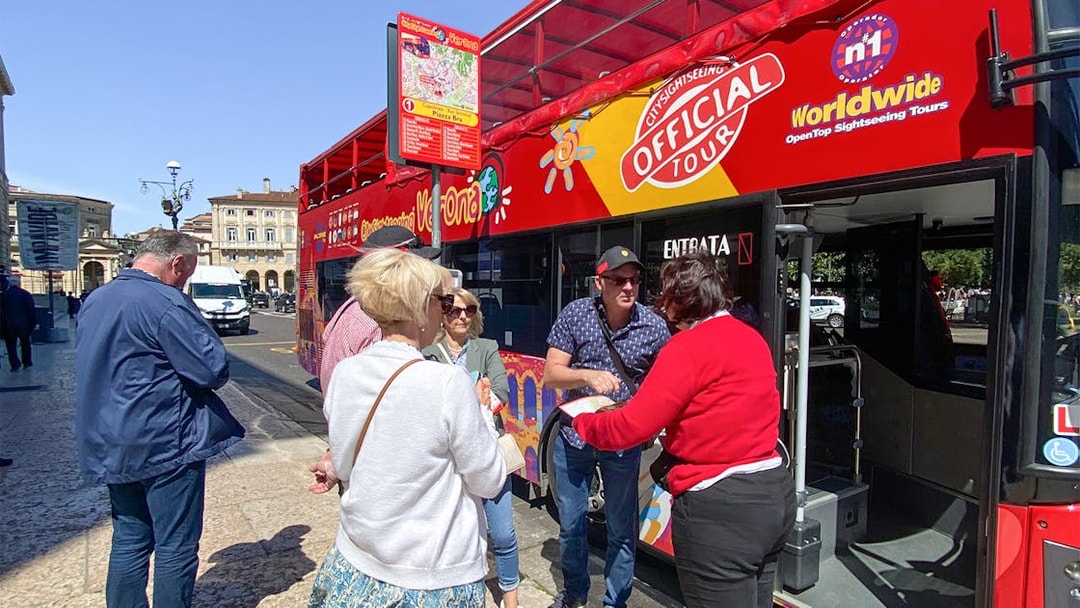 Tourists boarding a red hop-on hop-off bus in Verona for a sightseeing tour.