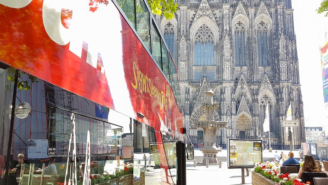 Hop on hop off bus near Cologne Cathedral with Gothic architecture in background.