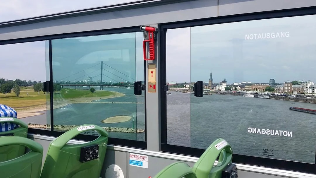 Open-top bus view of Rhine River and Dusseldorf skyline during hop-on hop-off city tour.