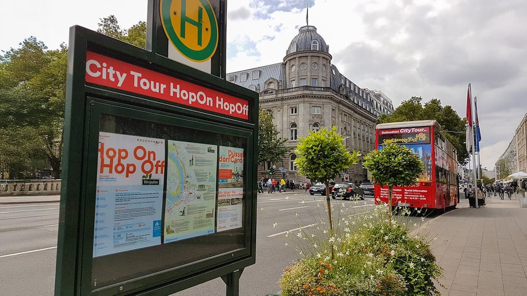 Hop-on hop-off bus stop with tour map and red double-decker bus in Düsseldorf.