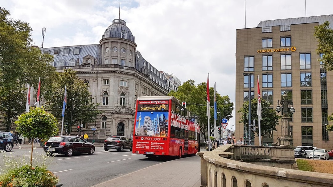Red double-decker bus on a city tour in Düsseldorf, passing historic buildings.