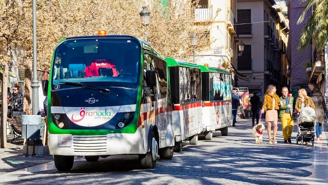 Granada city tour bus on a cobblestone street with people walking nearby.