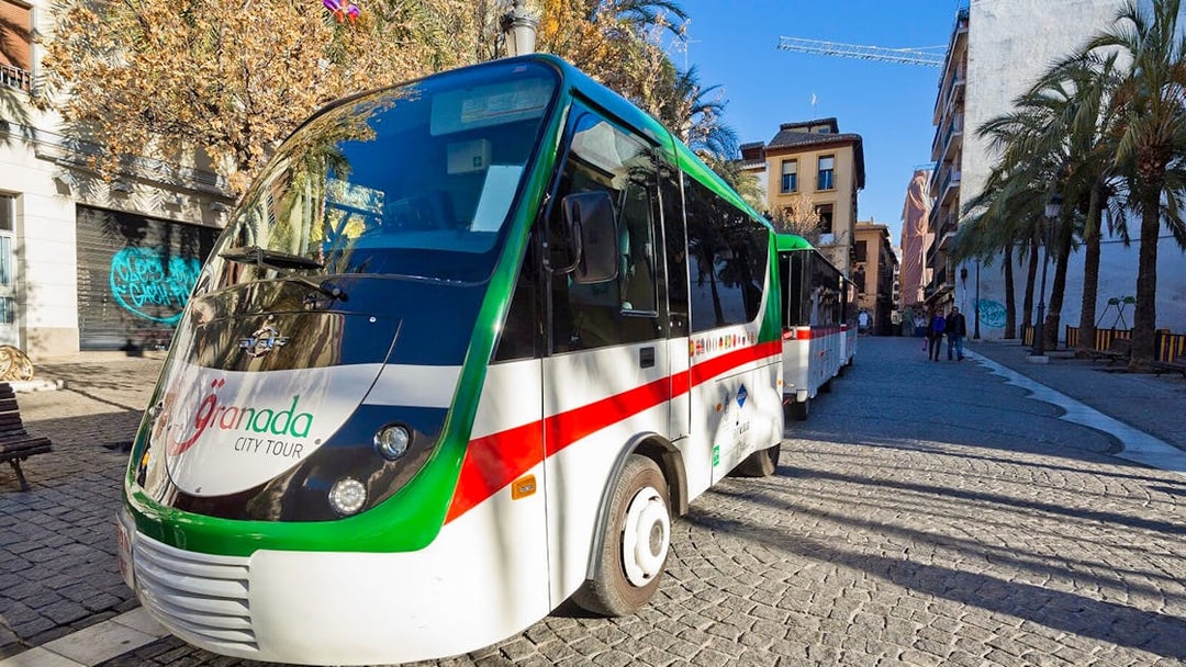 Granada city tour bus parked on a cobblestone street with palm trees.
