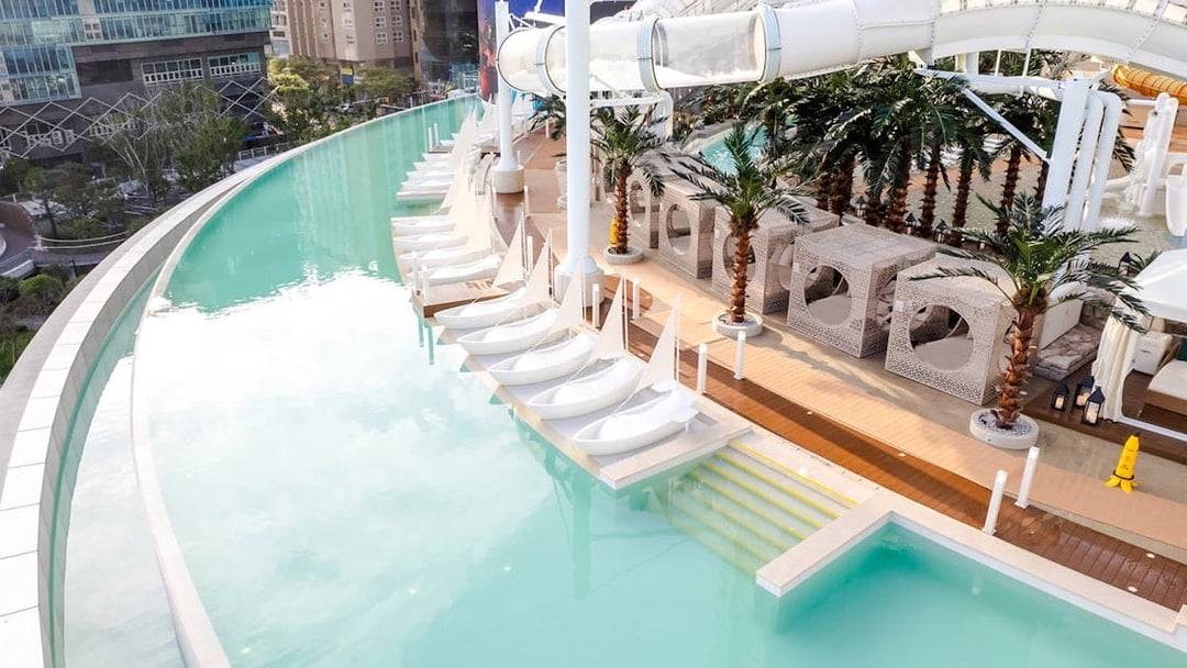 Rooftop infinity pool with sail-shaped loungers, cabanas, and waterslide at Club D Oasis.