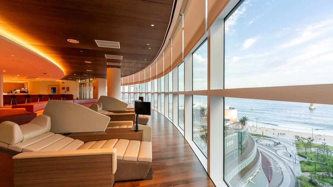 Indoor lounge at Club D Oasis with panoramic windows overlooking Haeundae Beach.
