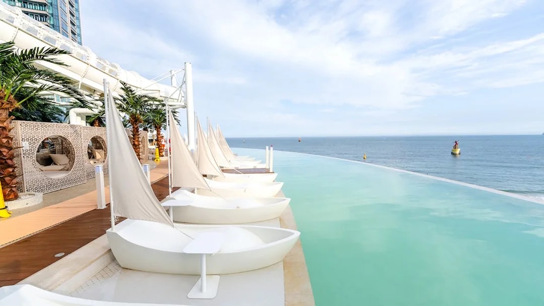 Boat-shaped sun loungers by Club D Oasis infinity pool with ocean view in Busan.