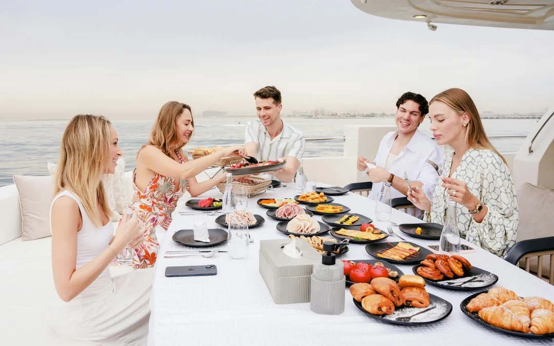 Visitors dining on a cruise in Dubai with a spread of pastries and cold cuts.
