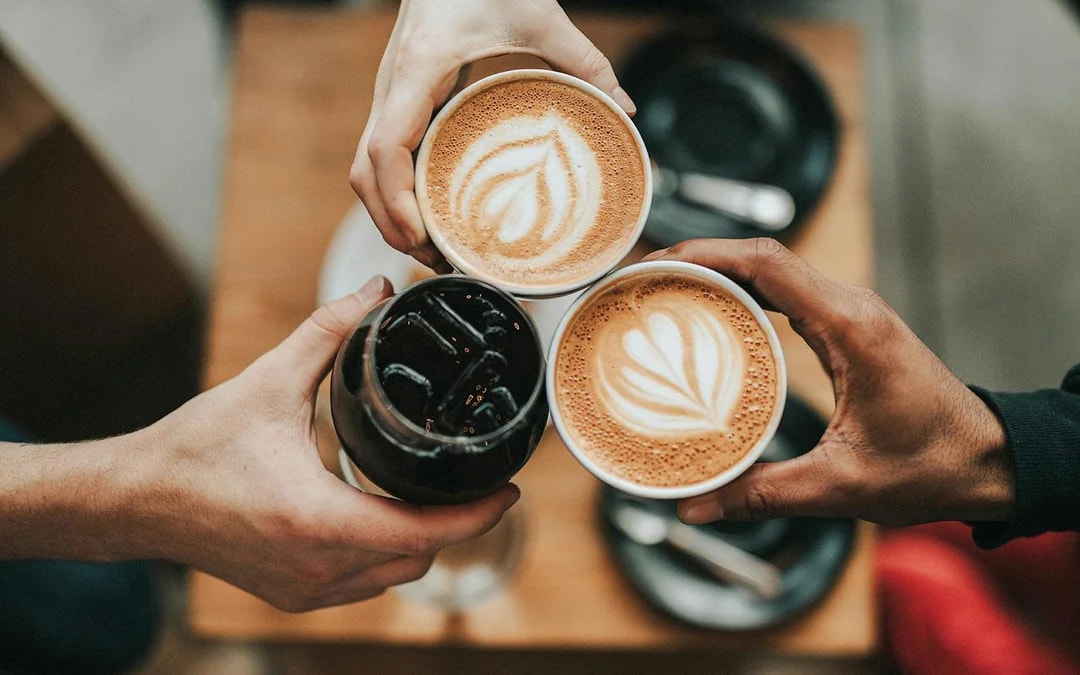 Visitors holding coffee cups with latte art and iced coffee.