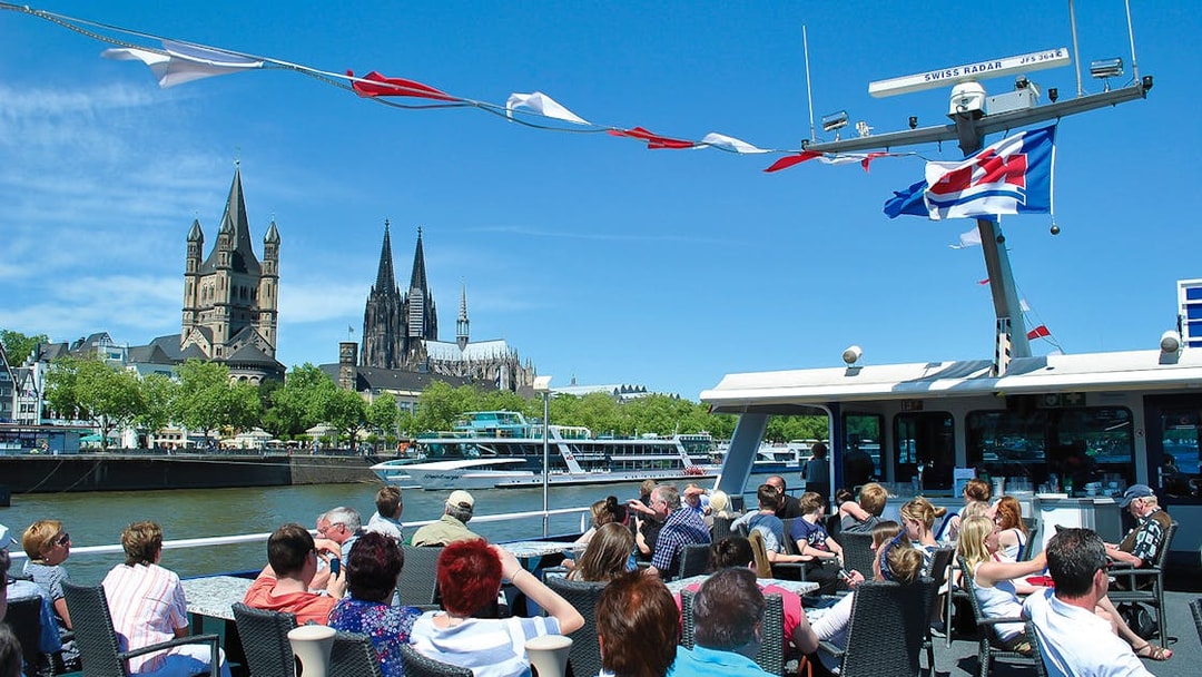 Tourists on a boat enjoying a panoramic view of Cologne Cathedral and Great St. Martin Church.
