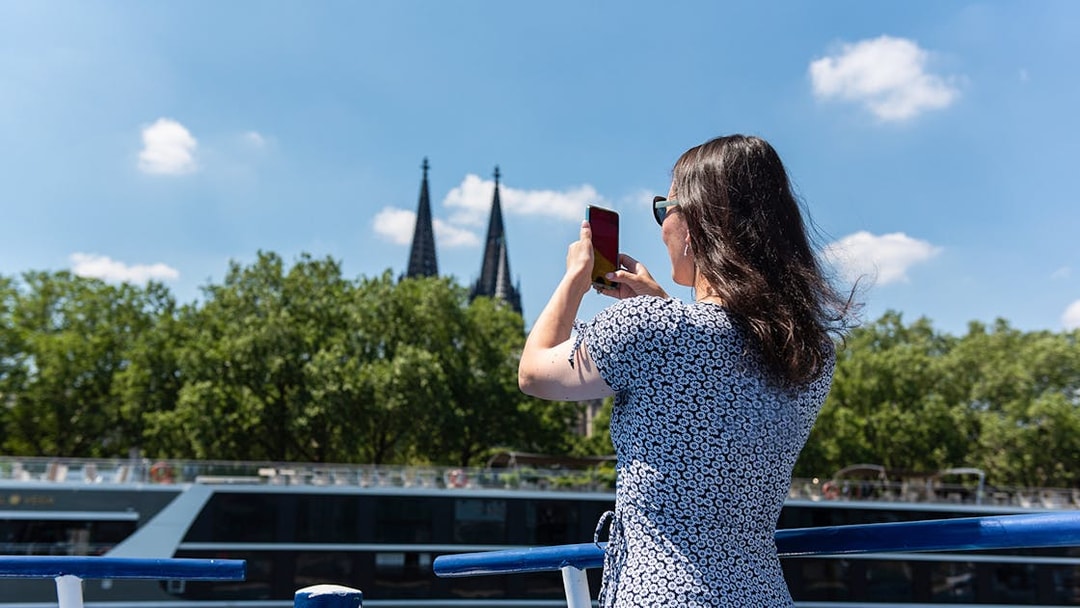 Person photographing Cologne Cathedral spires from a boat on the Rhine River.