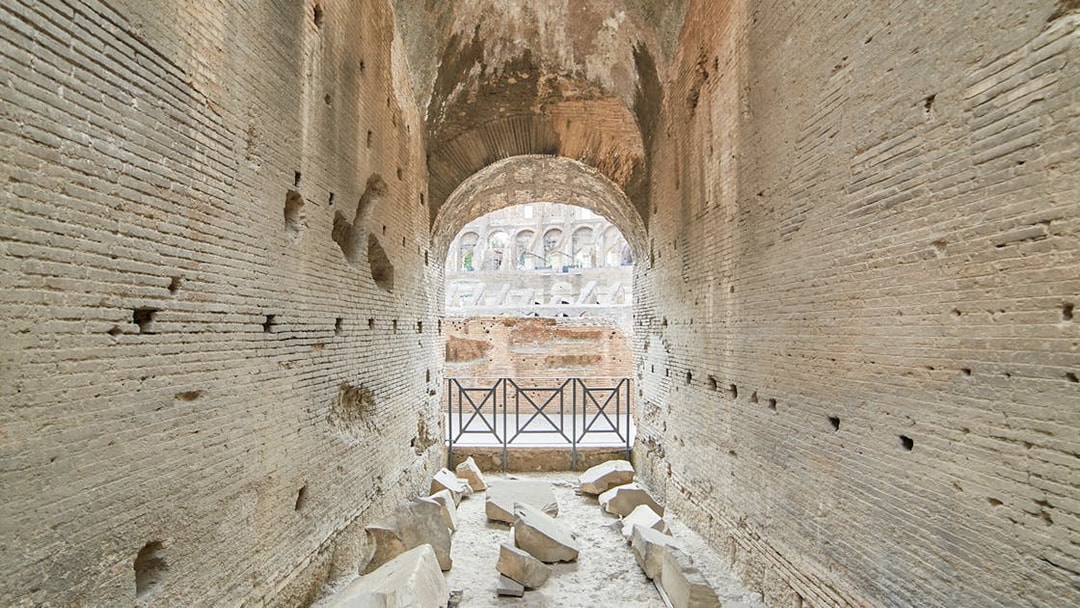 Archway passage in the underground Colosseum, Rome, with ancient stone walls and scattered ruins.