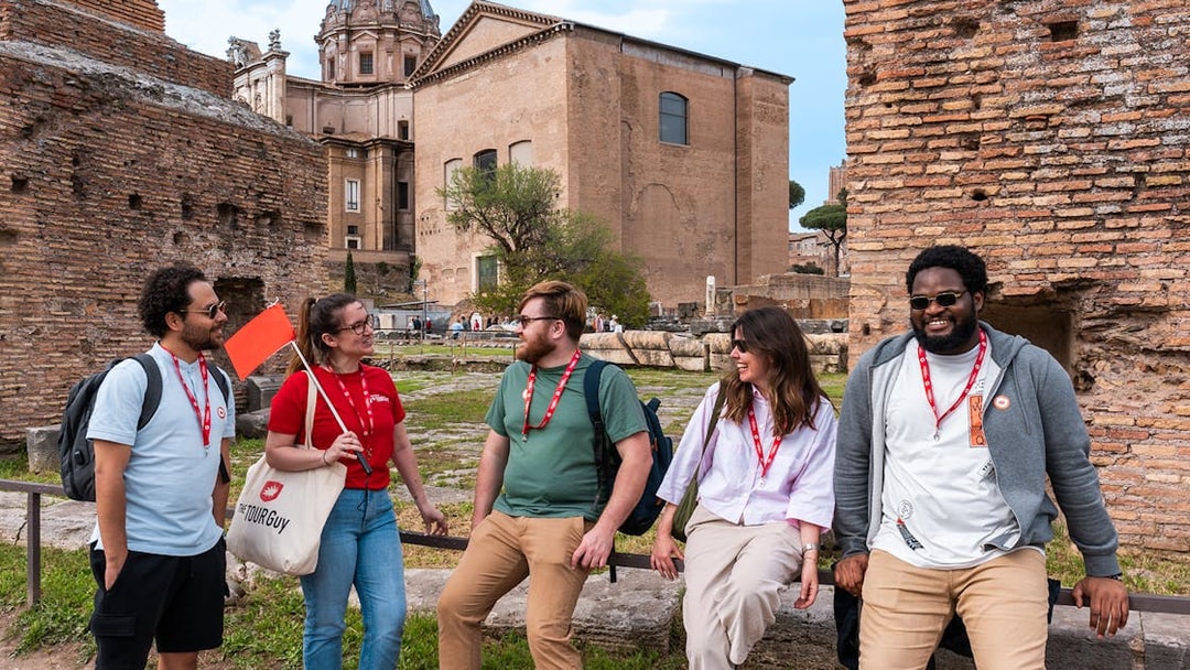 Tour group at Roman Forum with guide holding flag, ancient ruins in background.