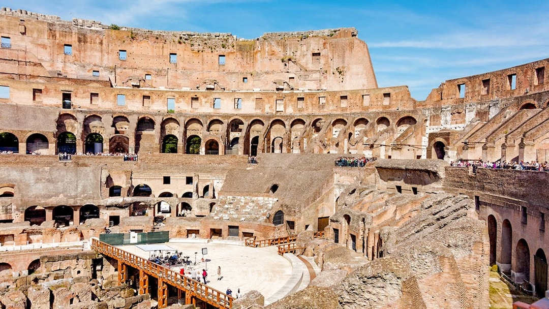 Tour group exploring the Colosseum Arena in Rome, viewing underground chambers and learning gladiator history.