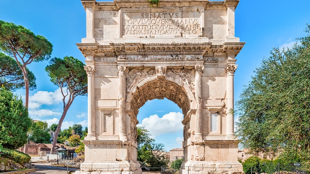 Arch of Titus with trees and blue sky in the Roman Forum, Rome, Italy.