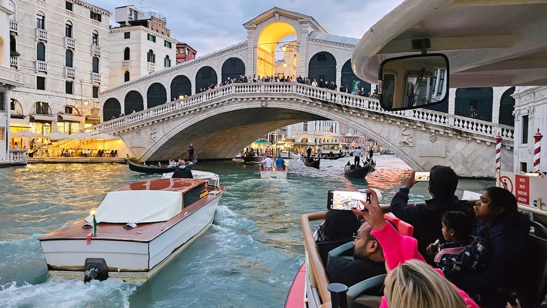 Vaporetto ACTV water bus passing under Rialto Bridge in Venice with tourists onboard.