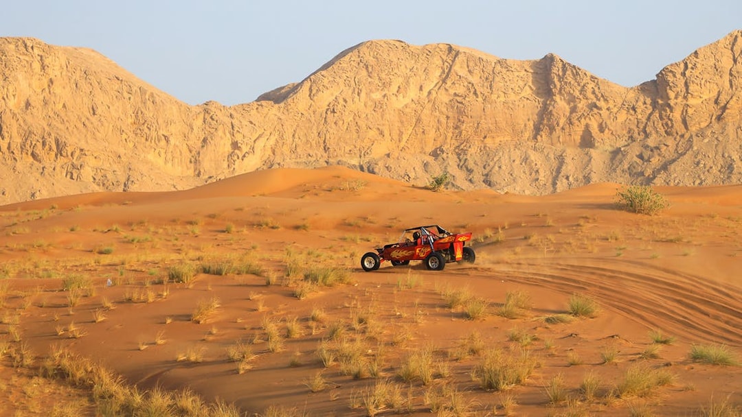 Dune buggy driving through Dubai's Red Dunes desert with rocky mountains in the background.