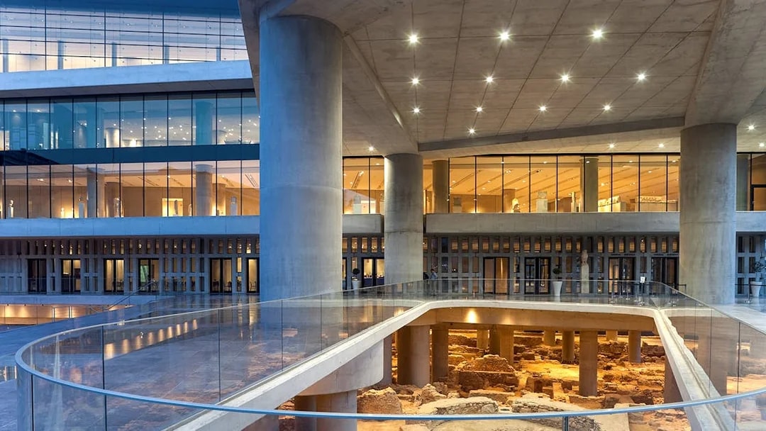 Corridor of Acropolis Museum with glass walkway and ancient ruins below.