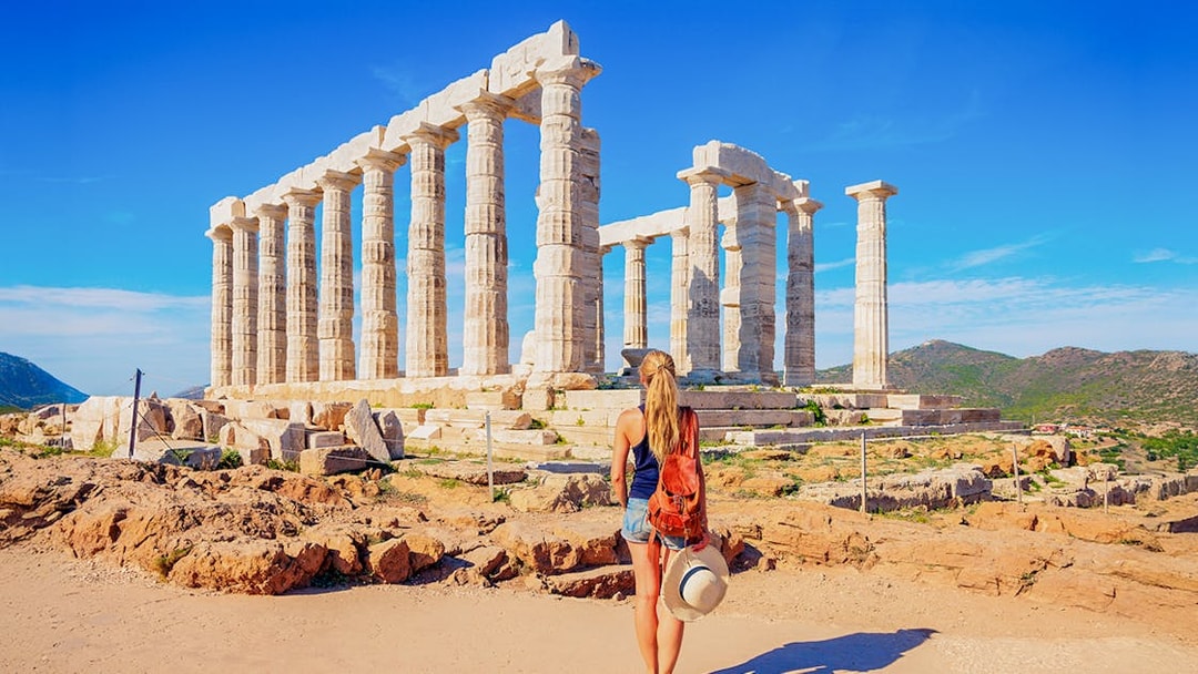 Visitor at the Temple of Poseidon, Greece, with ancient columns and scenic landscape.