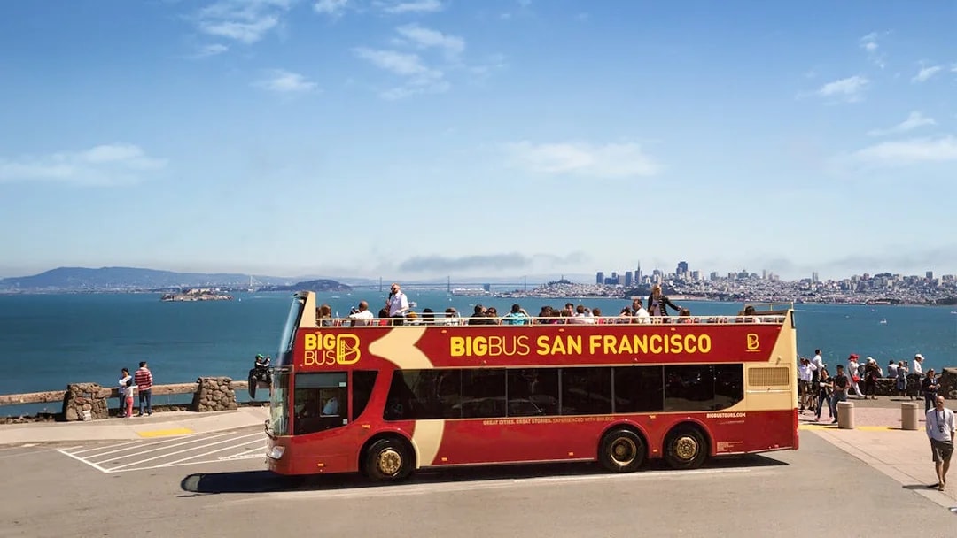 Open-top tour bus in San Francisco with city skyline and bay in the background.