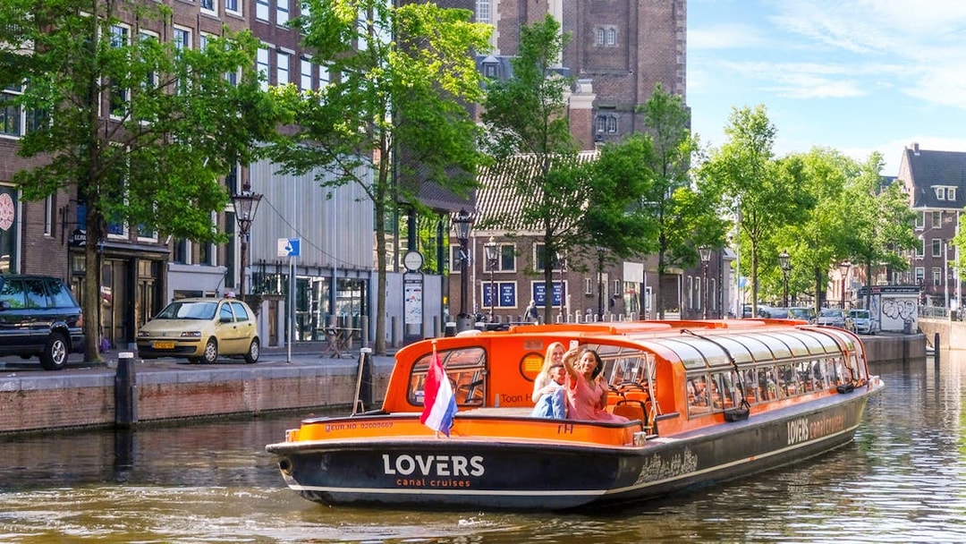 Canal cruise boat on Amsterdam canal with passengers taking photos.
