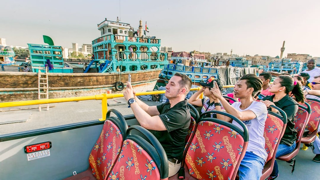 Tourists on a hop-on hop-off bus taking photos of Al Seef Dhow in Dubai.