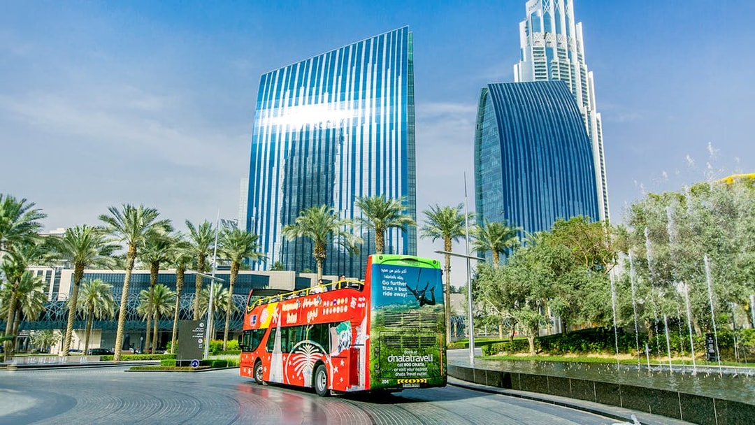 Open-top tour bus near modern skyscrapers in Dubai on Hop-On Hop-Off Tour with Al Seef Dhow Cruise.