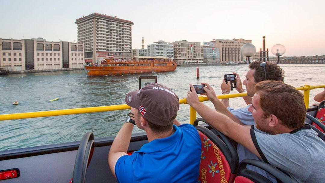 Tourists on HOHO bus photographing dhow cruise on Dubai Creek.