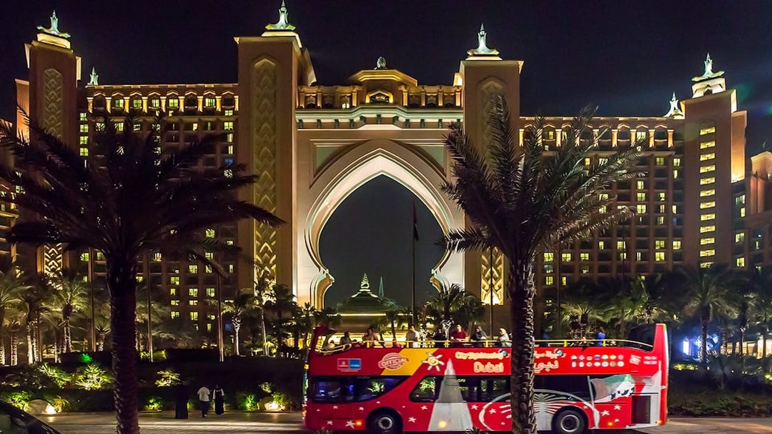 Open-top tour bus in front of Atlantis Hotel, Dubai at night.