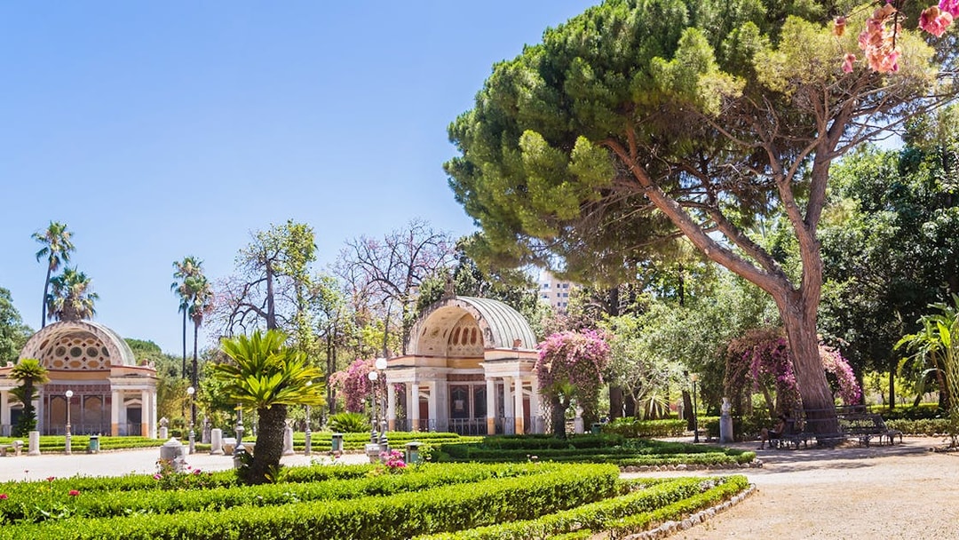 Orto Botanico garden with lush greenery and historic pavilion, Palermo, Italy.